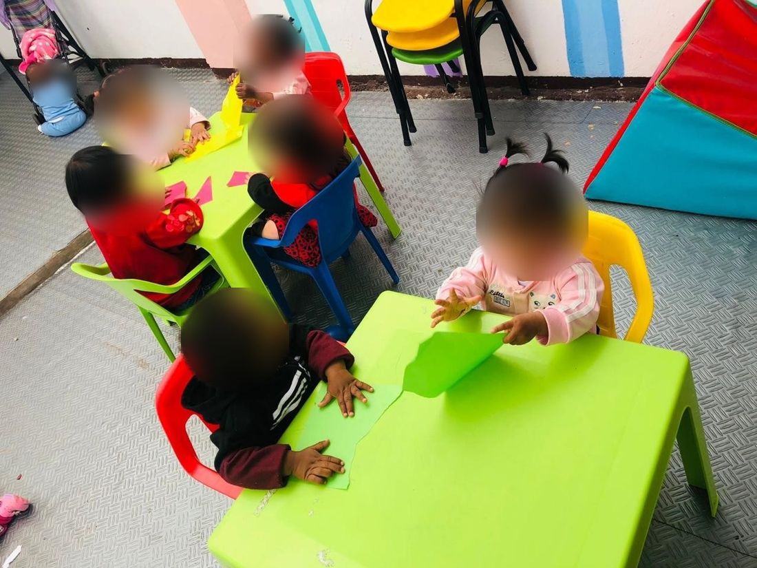 Grupo de niños de primera infancia en mesas de trabajo con papel de colores