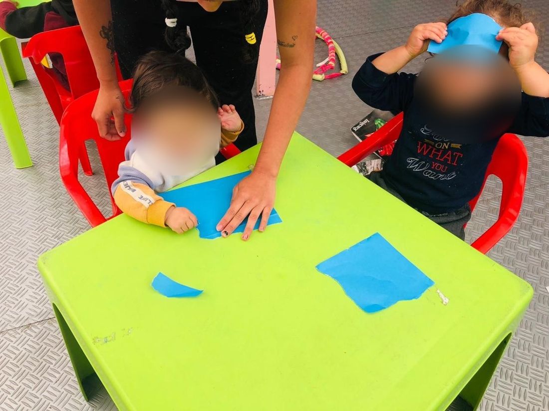 Educadora acompañando a dos niños pequeños en una actividad con papel
